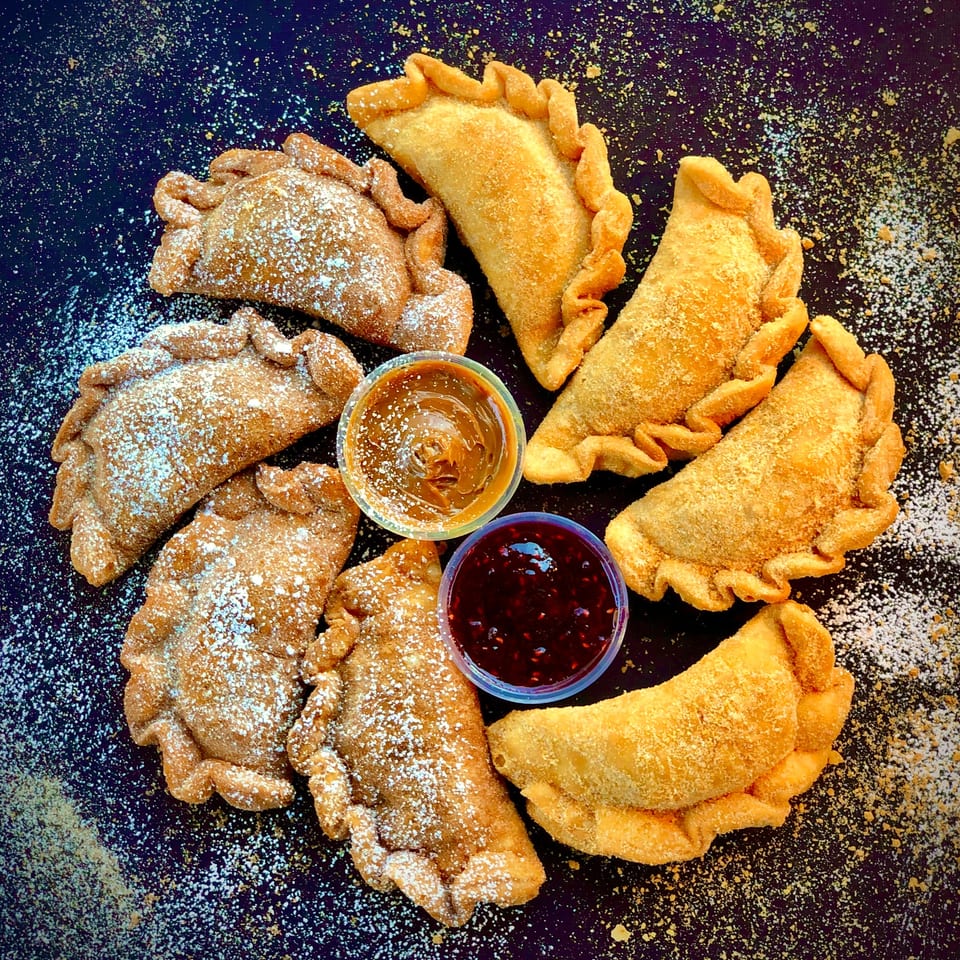 Sweet Lord Empanadas, some dusted with powdered sugar, arranged around dulce de leche and jam.