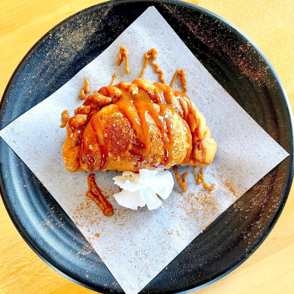 Dulce de leche empanada drizzled with caramel and a dollop of whipped cream on a black plate.