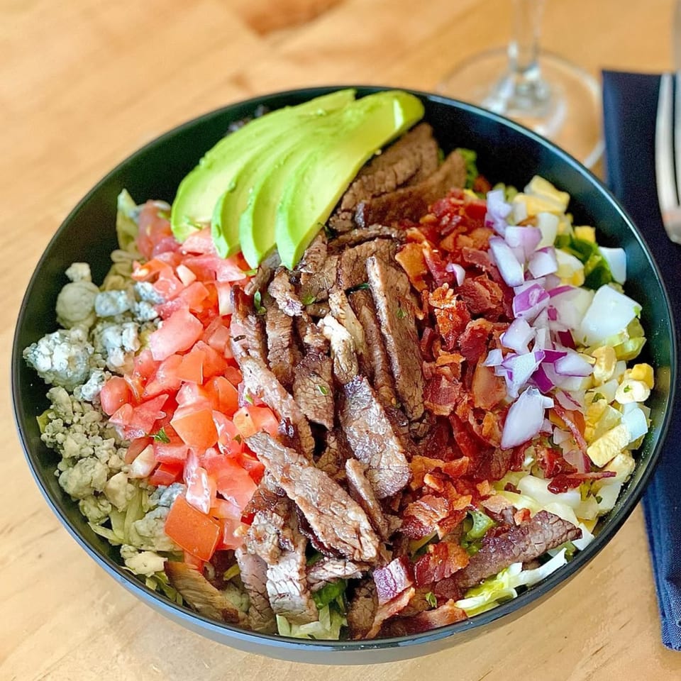 A vibrant Lord Empanada Cobb salad with steak, avocado, bacon, tomatoes, blue cheese, and eggs.