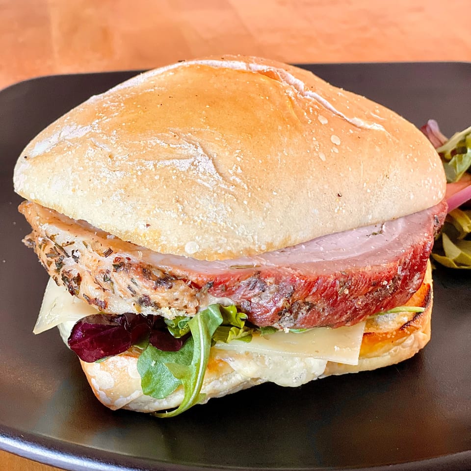 Close-up of a Lord Empanada sandwich with thick-cut meat, cheese, and greens on a bun.