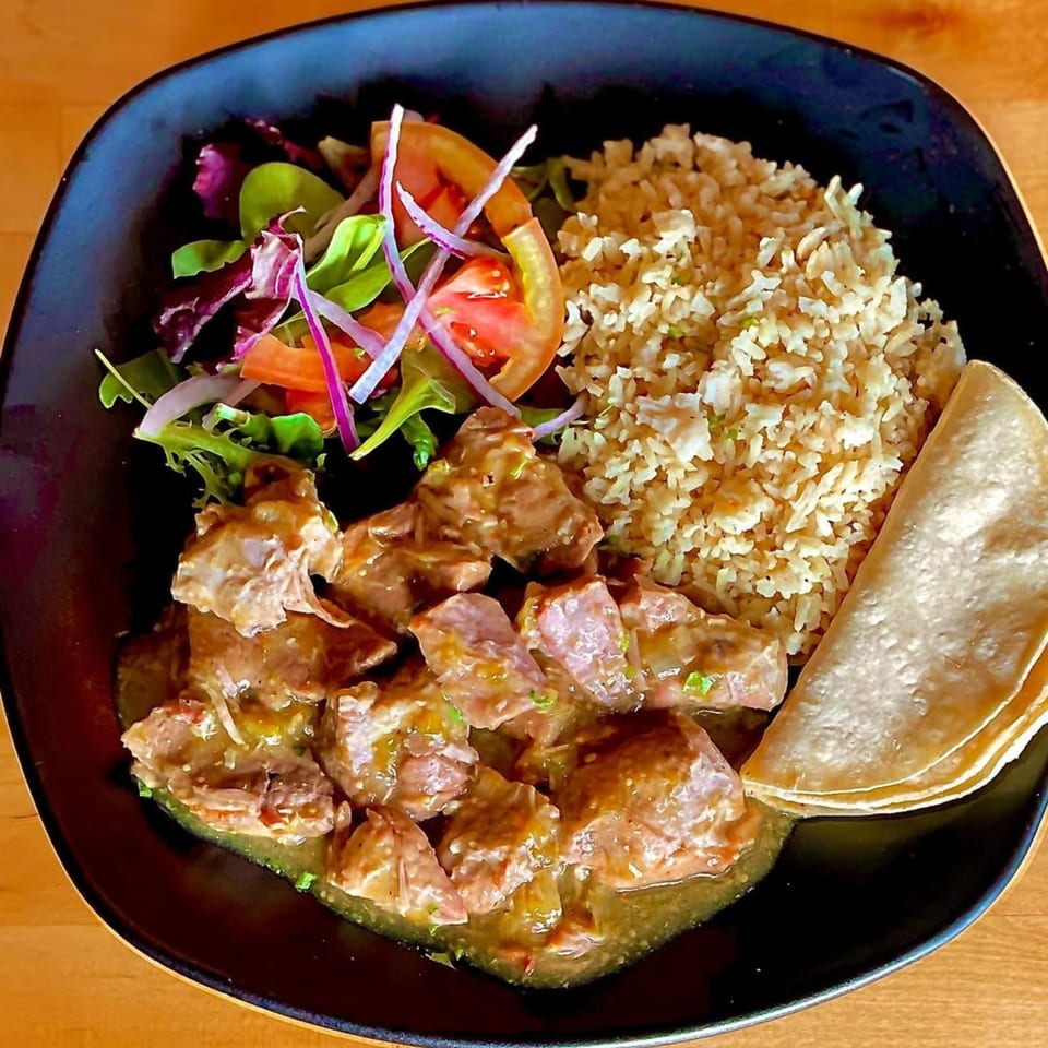 Argentinian pork stew with rice, salad, and tortillas on a black plate.