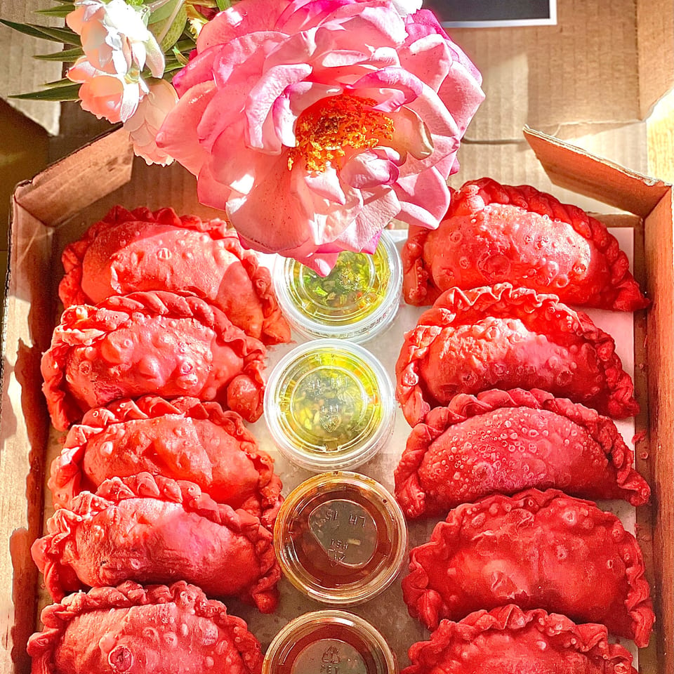 Red empanadas and dipping sauces in a cardboard box, with a pink rose.