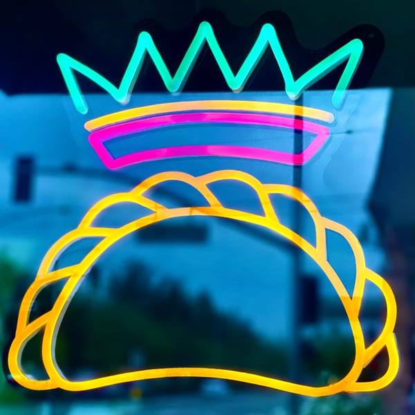 Neon sign of a yellow empanada with a pink and yellow crown, against a blue background.