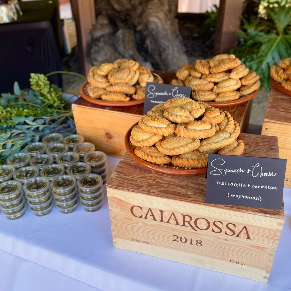 Plates of golden-brown spinach and cheese empanadas with small sauce containers on a white table.