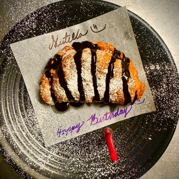 Nutella empanada drizzled with chocolate and powdered sugar, with a red candle and "Happy Birthday" text.