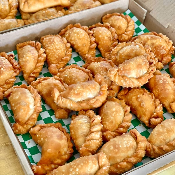 A box filled with golden-brown, freshly baked Lord Empanada pastries on green and white checkered paper.