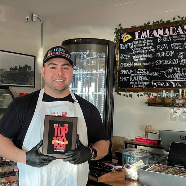 Lord Empanada owner proudly holding a "Yelp Top 100 Places to Eat" award in his restaurant.