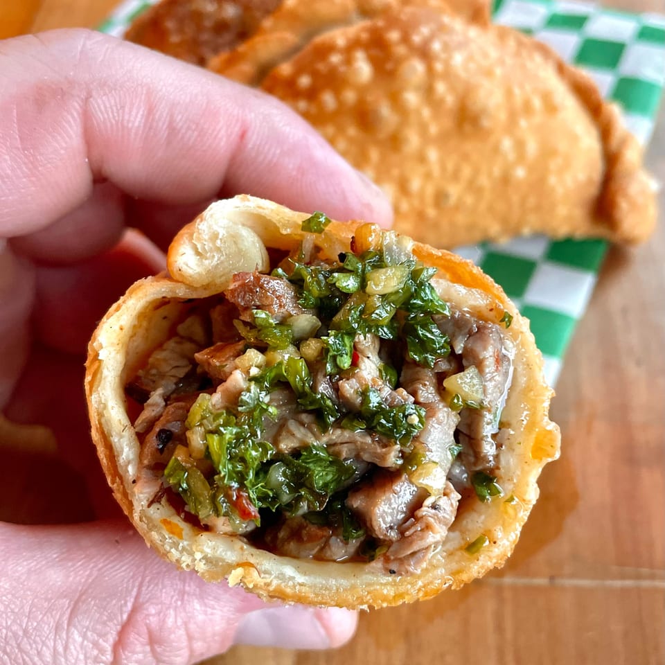 Hand holding a Lord Empanada, cut open to show steak and chimichurri filling.