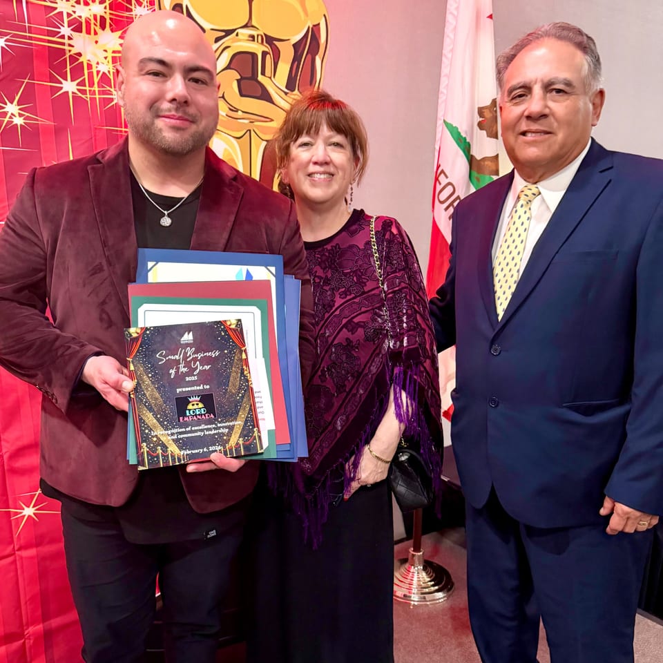 Three people, including the owner of Lord Empanada, posing with a "Small Business of the Year" award.