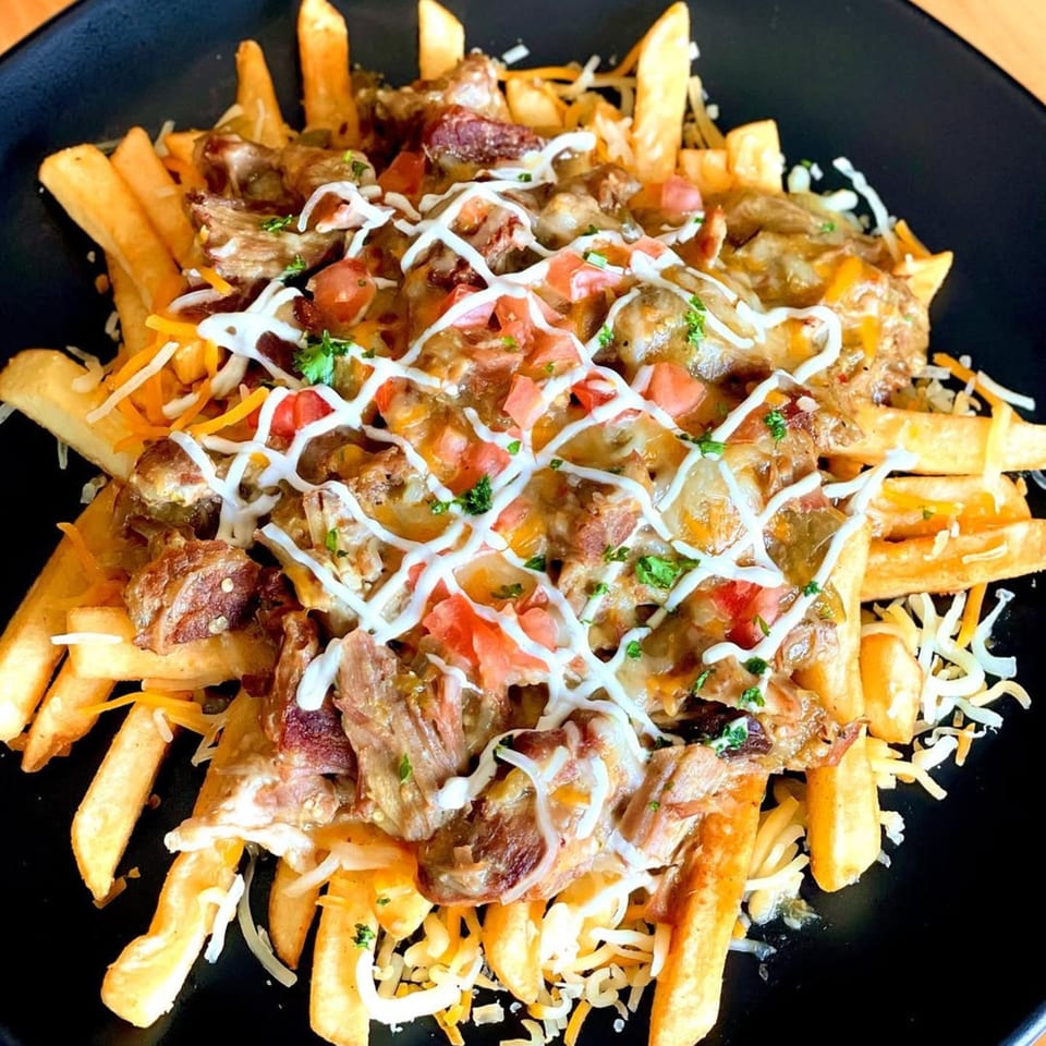 Lord Empanada's loaded fries with meat, cheese, tomatoes, and a drizzle of white sauce.