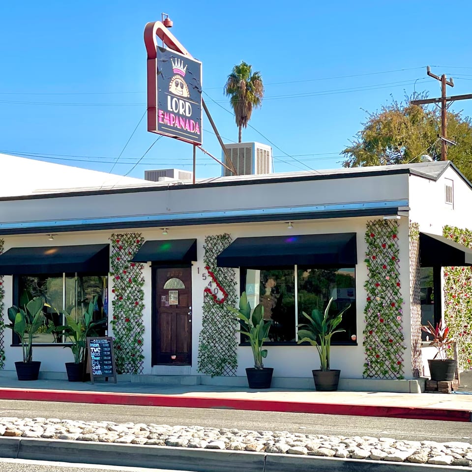 Exterior of Lord Empanada restaurant with a prominent sign, black awnings, and decorative trellises.